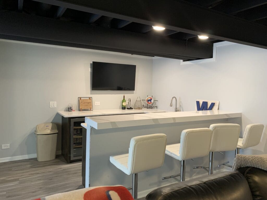 Image of a basement renovation featuring bar and barstools with small kitchen.