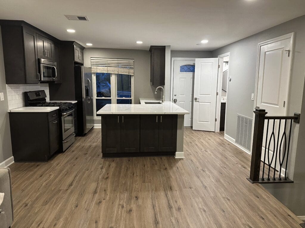 contemporary kitchen features warm wood laminate flooring, dark brown cabinets, and white countertops