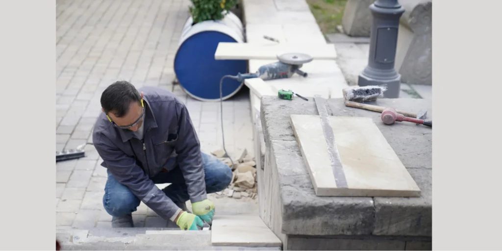 A worker carefully cuts and fits stone tiles on outdoor steps during a deck installation service, showing detailed craftsmanship and preparation work