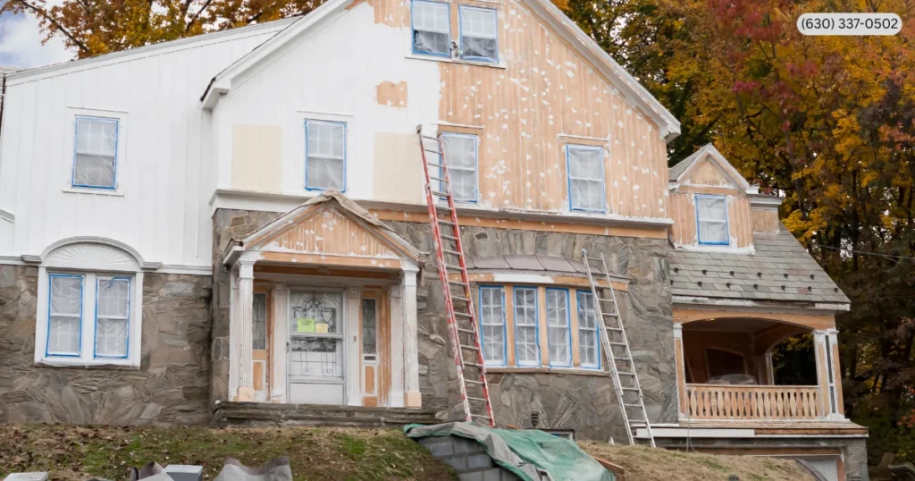 Large residential home undergoing renovation with ladders, partially stripped siding, and protected windows, showcasing professional Exterior Home Improvement Services, exterior remodeling, home restoration, and property upgrades. 