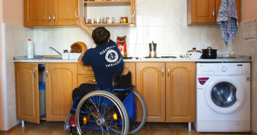 A person in a wheelchair grabbing kitchen cabinets in a Wheelchair Accessible Kitchen with lowered countertops and accessible storage for independent daily living.  