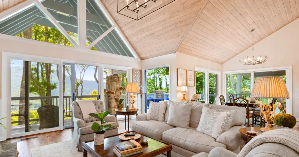 Open, spacious bright living room with white walls and large windows, neutral furniture, vaulted wood ceiling, What Colors Make Your Room Look Bigger. 