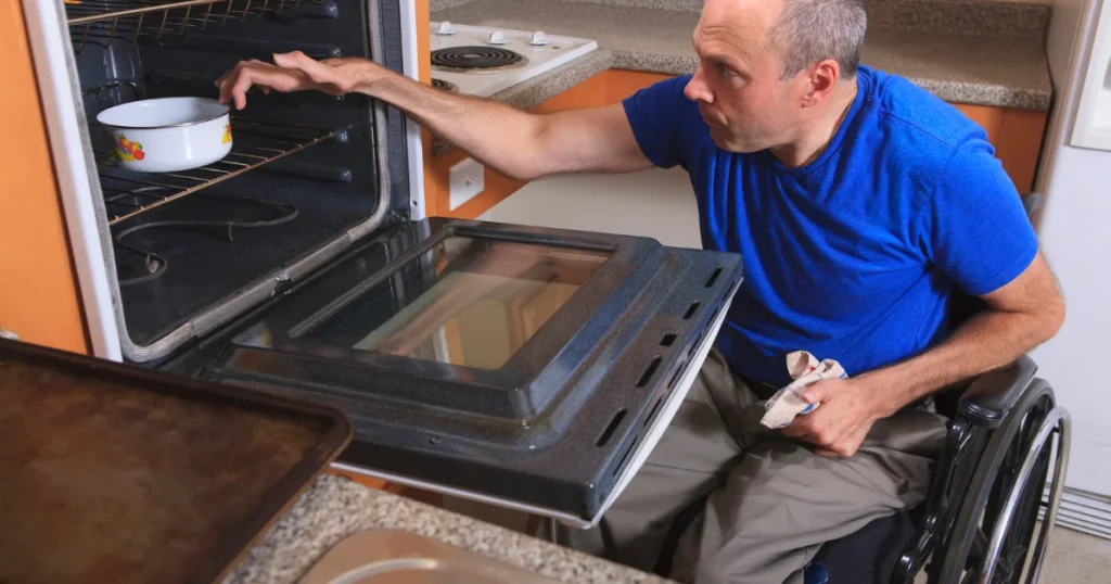 Wheelchair Accessible Kitchen with accessible appliances and a functional kitchen layout for greater independence, wheelchair user safely taking a dish out of an oven. 